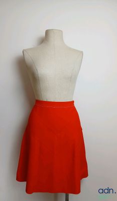 une jupe orange posée sur un mannequin, devant un mur blanc