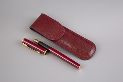 burgundy leather pen case with gold accents and a red ballpoint pen