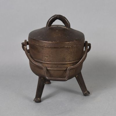 an old metal pot with a handle on a stand on a gray surface