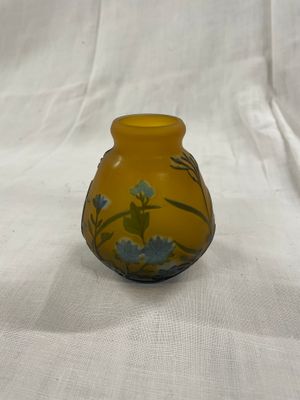 un vase jaune orné de fleurs bleues, posé sur une nappe blanche