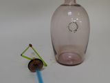 a pink glass bottle with a blue handle next to a small glass object
