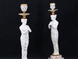 a pair of white and gold candlesticks with statues on them