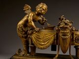 bronze statue of a cupid preparing a meal on a table