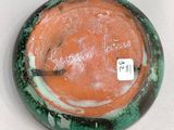 a green and orange vase with a white label on it
