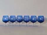 six verres à vin bleus alignés sur une surface blanche