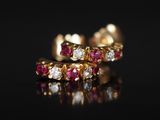 une paire de boucles d'oreilles créoles en rubis et diamants posées sur un fond noir