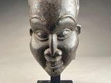sculpture représentant le visage d'une femme, posée sur un socle, avec un fond gris