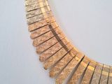 the necklace is made of gold metal and has a curved design on it