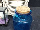a blue glass jar with a cork lid next to a stack of white plates