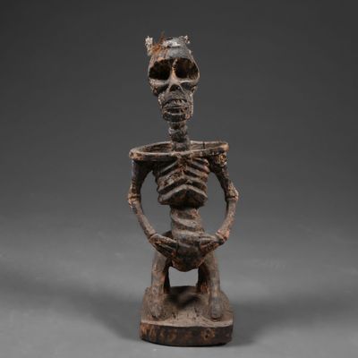 une statue en bois représentant un squelette tenant une tête humaine