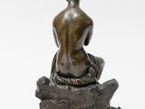 a bronze statue of a woman sitting on a rock with her back to the camera