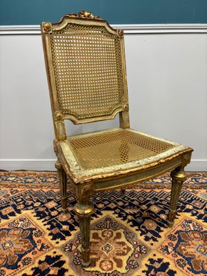 an antique chair with gold paint and wicker seat on a rug