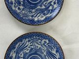 two blue and white plates with designs on them sitting on a table