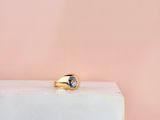 une bague en or sertie d'une topaze bleue repose sur un bloc blanc