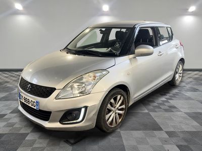 Une Suzuki Swift argentée est garée dans une pièce au sol à carreaux.