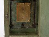 a small green clock with a brass plate in the middle