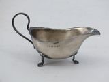 an antique silver plated sauce boat with a handle on a stand