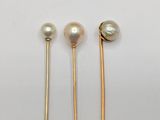 three gold and pearl pins on a white background