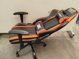 an orange and black gaming chair sitting on top of a desk