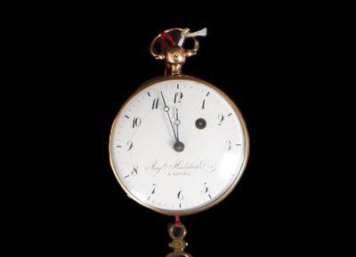 a gold clock hanging from a chain on a black background