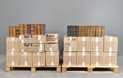 Deux piles de livres sont empilées sur des palettes devant un mur gris.