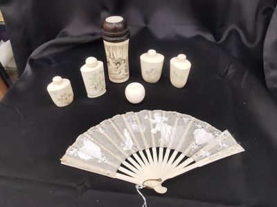un éventail et un flacon de parfum posés sur un tissu noir