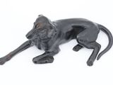 statue of a black dog laying down on a white surface