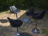trois tabourets de bar en cuir noir posés dans l'herbe, à côté d'un buisson