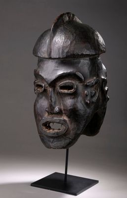 un masque en bois posé sur un socle, sur fond gris