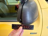 a person holding a ruler in front of a yellow car
