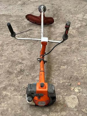 an orange string trimmer on the ground next to a pair of shoes