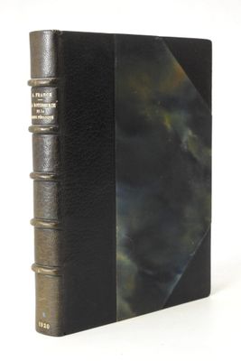 an old book with a black cover sitting on top of a white table