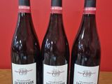 trois bouteilles de vin posées sur une table devant un mur rouge