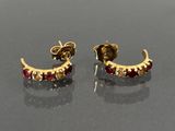 une paire de boucles d'oreilles en or et rubis posées sur un fond noir