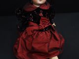 an old doll with a red dress and black shoes sitting on a black surface