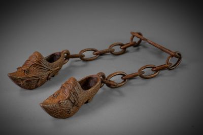 pair of wooden shoes hanging from a chain on a gray surface