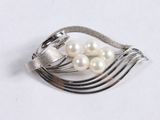 a silver brooch with pearls on it on a white surface