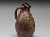 un vieux vase marron muni d'une anse, posé sur un fond blanc