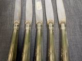 quatre couteaux en métal argenté et un porte-couteaux posés sur une table