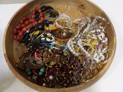 un bol en bois rempli de bijoux variés, posé sur une table