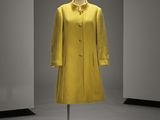 un manteau jaune posé sur un porte-manteau dans une pièce aux murs blancs