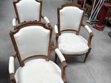 trois chaises blanches posées sur un sol en béton, à côté d'un tas de bric-à-brac