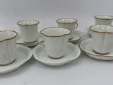 six white and gold coffee cups and saucers on a white table