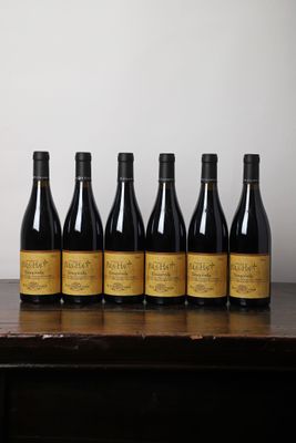 six bouteilles de vin sont posées sur une table devant un mur blanc