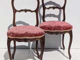 pair of antique chairs with red upholstered cushions against a white wall