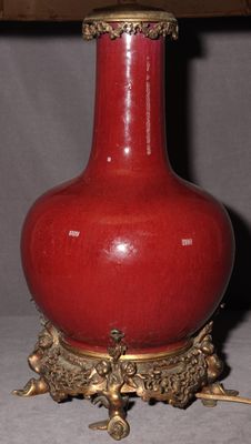 un vase rouge posé sur une table sur laquelle se trouve une lampe