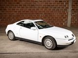 a picture of a white car parked in front of a brick wall