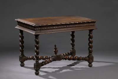 une vieille table en bois dont le plateau est sculpté, sur fond gris