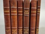 six livres en cuir marron alignés les uns à côté des autres sur une surface blanche