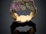 un gros plan sur une bague en or sertie de pierres roses et vertes